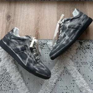 Gråsvarta gats från Maison Margiela - Unika sneakers från Maison Margiela i gråsvart färg med vit tvättad effekt. Lågt skaft, vita skosnören och svart sula. Tillverkade i läder och mocka för en lyxig känsla och cool look. Kommer i originalkartong.