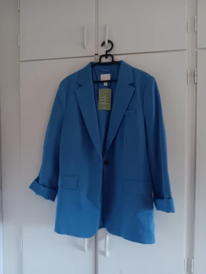 Blå oversized kavaj - Stilren blå oversized kavaj med klassisk krage och enkelknäppning.  Ärmarna är uppvikta för en avslappnad look men går att rulla ner Perfekt för att lyfta vilken outfit som helst.