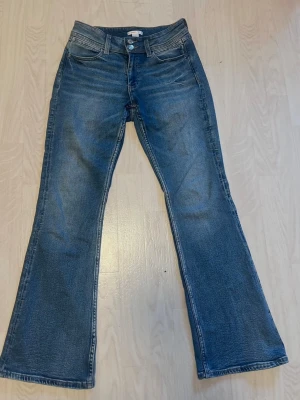 Blå bootcut jeans med broderade fickor - Säljer ett par blå bootcut jeans  broderade detaljer på bakfickorna. Jeansen har klassisk femficksmodell, normal/låg midjade och stängs med två knappar och dragkedja. Köptes på Gina Young för 359 och är i storlek 164 men passar mig som vanligtvis jag S och är ca 162cm Perfekta för dig som gillar en avslappnad men trendig look.