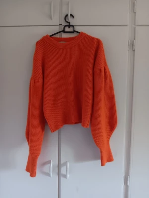 Orange stickad tröja - Säljer en  stickad tröja i stark orange färg. Tröjan har breda, långa ärmar och ribbstickad struktur med rund halsringning. Perfekt för dig som vill ha en färgklick i garderoben och gillar en avslappnad, trendig stil.