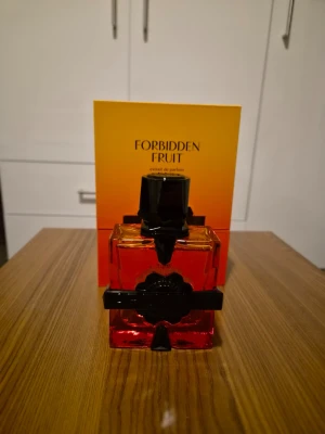 Forbidden Fruit parfym byte / sälj - Forbidden Fruit extrait de parfum i en fyrkantig glasflaska med röd-orange toning och svart dekorativ kork. Flaskan har en elegant svart etikett och detaljer som ger en lyxig känsla. Perfekt för dig som gillar unika och djärva dofter.