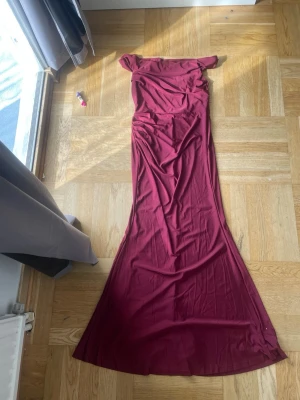 Vinröd långklänning offshoulder - Säljer en elegant vinröd långklänning med offshoulder-design. Klänningen har en figurnära passform upptill och faller snyggt längs kroppen. 