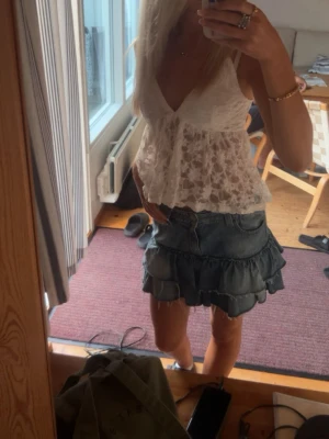 Vit spetsig linnetopp med volang - Supersöt vit linnetopp med tunna axelband och v-ringning. Toppen är täckt av blommig spets och har volangig nederkant som ger en romantisk känsla. Perfekt att styla med jeans eller kjol för en trendig look.använd en gång