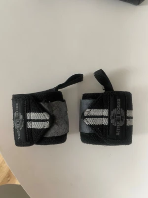 Svarta Wrist wraps (Handledslinor) från Better Bodies - Wrist wraps från Better Bodies i strl OneSize. Köpa för 200 kr, säljes för 50 kr exkl. frakt. Lite missfärgade pga tvätt och flera års användning, därav priset. Säljes pga att de ej kmr till användning längre. Använder dem knappt längre då jag upplever att jag är starkare i handlederna nu, än när jag började gymma. Kan fraktas eller mötas upp i Göteborg! Finns på fler sidor!