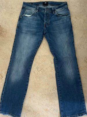 Blå raka jeans från LTB - Snygga blå jeans från LTB med raka ben och klassisk femficksdesign. Jeansen har en lätt tvättad look med slitningar vid fickorna och bakfickor med dekorativa sömmar. Perfekta för en avslappnad stil och passar till det mesta.