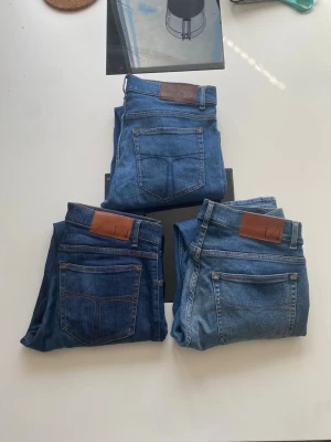 3-pack blåa jeans från Tiger of sweden  - Säljer tre par klassiska blå jeans från Nudie Jeans i olika tvättar. Alla har fem fickor, raka ben och läderpatch bak i midjan. Perfekta för dig som gillar stilrena och tidlösa jeans med snygg passform.