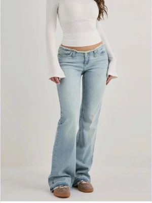 Ljusblå lågmidjade jeans  - Säljer ett par ljusblå bootcut jeans med låg midja och klassisk femficksdesign. Jeansen har en avslappnad passform över låren och utsvängda ben. Perfekta för en trendig och avslappnad stil. Materialet är mjuk denim i bomull.