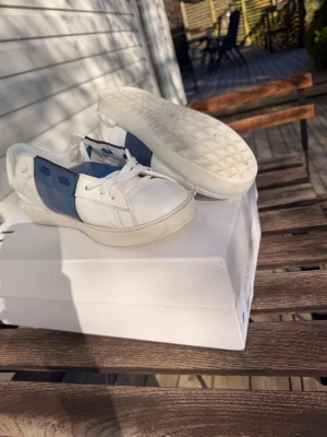 Vita och blå sneakers från Valentino - Skriv privat för kvitto eller flera bilder!!!! Snygga sneakers från Valentino open i vitt läder med blåa detaljer på sidan och blåa öljetter. Klassisk låg modell med vit sula och vita skosnören. Perfekta för en clean och stilren look.