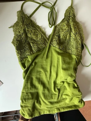 Grön spetsbody med halterneck - Snygg grön body med spets upptill och halterneck-band. Djup v-ringning med blommönstrad spets och mjukt tyg nedtill. Perfekt för dig som gillar att sticka ut med färg och detaljer. Passar dig som vill ha något både bekvämt och trendigt.