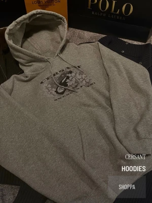 Grå hoodie från Cersant med tryck - Snygg grå hoodie från Cersant med ett stort tryck på bröstet som visar blommor och text. Hoodien har klassisk huva med dragsko och en avslappnad passform. Perfekt för en chill och casual stil.