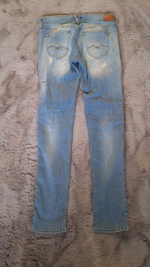 Replay Rose ljusa ripped jeans 29/32 - Säljer ett par ljusblå jeans från Replay, modell Rose, med snygga slitningar och ripped detaljer framtill. Klassisk femficksdesign, knappstängning och coolt Replay-märke vid fickan. Perfekt för dig som gillar en avslappnad streetstil.