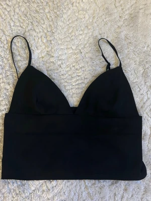 Svart bralette med smala axelband - En stilren svart bralette med smala, justerbara axelband och mjuka triangelformade kupor. Modellen är utan bygel och har en bred resår under bysten för extra komfort. Perfekt för en enkel och modern look. Köpt från bikbok i storlek xs 