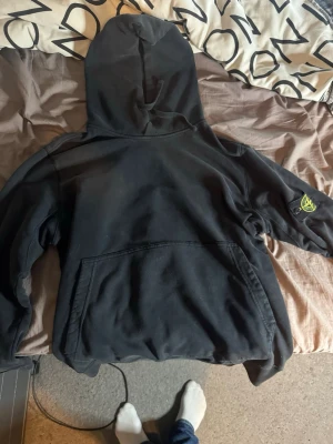 Svart hoodie från Stone Island - Svart hoodie från Stone Island med klassisk logotyp-patch på vänster ärm. Hoodien har stor huva och en rymlig magficka framtill. Tillverkad i mjukt bomullsmaterial som är skönt att bära. Perfekt för en avslappnad streetwear-look.