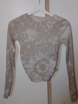 Beige ribbad långärmad tröja från Kappahl - Långärmad tröja från Kappahl i beige med vitt batikinspirerat mönster. Tröjan har ribbad struktur, rund hals och smal passform. Storlek 170, tror inte att jag använt den, så bra kvalitet 