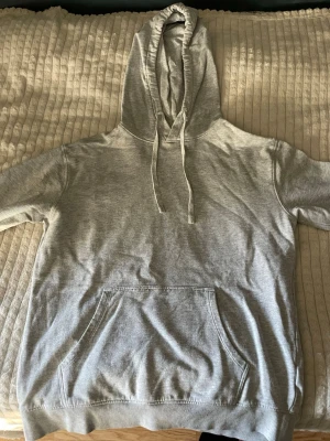 Grå basic hoodie med ficka - Enkel och stilren grå hoodie med huva och dragsnören. Har en stor magficka framtill och ribbade muddar vid ärmslut och nederkant. Perfekt för en avslappnad och chill look. Materialet känns mjukt och bekvämt, troligen bomullsblandning.Hoodien är använd fåtals gånger men inga desvidare defekter.