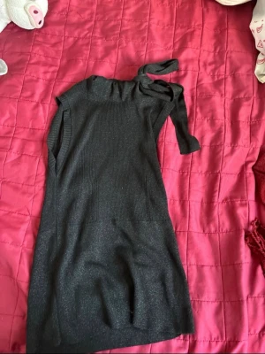 Svart glittrig oneshoulder topp - Stilren svart oneshoulder topp med glittrig finish och ribbad struktur upptill. Toppen har ett snyggt knyt vid axeln och är ärmlös, vilket ger en trendig look. Materialet känns stretchigt och bekvämt, perfekt för att lyfta din outfit. Skulle ändå säga mer onesize
