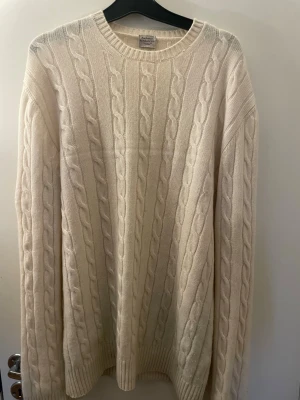 Vit kabelstickad cashmeretröja - Exklusiv vit kabelstickad tröja från Rose & Born i 100% cashmere. Tröjan har rund halsringning, långa ärmar och ribbade muddar. Perfekt för dig som gillar klassisk och stilren design med lyxig känsla.