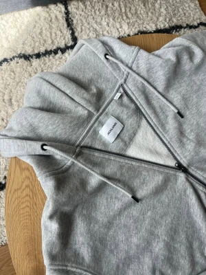 Grå zip hoodie från Jack & Jones - Tjena👋 Snygg gråmelerad hoodie från Jack & Jones med dragkedja framtill, huva med dragsnören och två fickor🤩 Tillverkad i mjukt sweatshirtmaterial som är perfekt för chill dagar✌️ Klassisk passform och ribbade muddar vid ärmar och nederkant👌 meddela gärna vid frågor📩