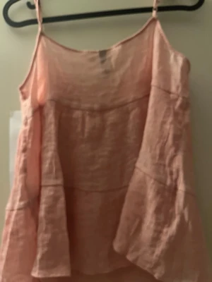 Ljusrosa linnetopp från H&M Divided - Söt ljusrosa linnetopp från H&M Divided med tunna axelband och flowig passform. Toppen är tillverkad i ett lätt och luftigt material, perfekt för varma dagar. Enkel och stilren design som är lätt att matcha med olika outfits.