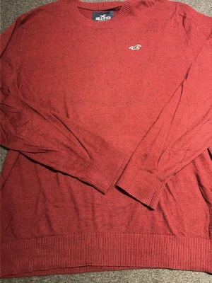 Röd tröja från Hollister - Röd långärmad tröja från Hollister med rund halsringning och diskret logga broderad på bröstet. Tröjan har ribbade muddar vid ärmslut och nederkant. Perfekt för en avslappnad och stilren look.