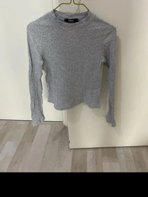 Grå ribbstickad tröja Bik Bok - Säljer en grå ribbstickad tröja från Bik Bok med rund halsringning och långa ärmar. Tröjan är figurnära och har en klassisk, enkel design som passar perfekt till jeans eller kjol.