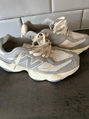 New Balance 9060 gråvita sneakers - Chunky sneakers från New Balance i modellen 9060. Skorna är gråvita med stora N-loggor på sidorna, meshpaneler och detaljer i mocka. Tjock sula för extra komfort och retrovibe. Perfekta för dig som gillar streetwear och vill ha en clean look.