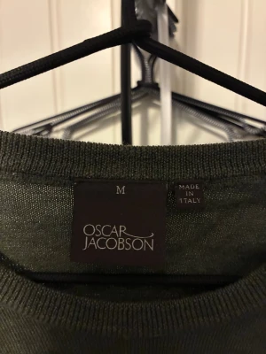 Mörkgrön stickad tröja Oscar Jacobson - Snygg mörkgrön stickad tröja från Oscar Jacobson. Tröjan har rund halsringning, långa ärmar och ribbade muddar vid ärmslut och nederkant. Tillverkad i Italien och passar perfekt för en stilren look.