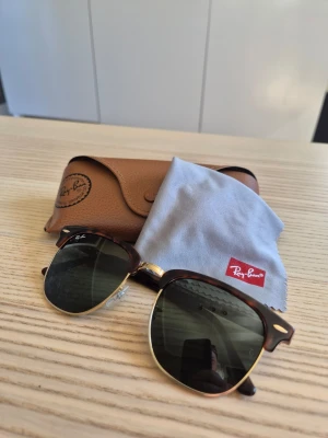 Ray-Ban Clubmaster solglasögon brun - Snygga Ray-Ban Clubmaster solglasögon med brunsköldpaddsmönstrad båge och guldiga detaljer. Kommer med originalfodral i brunt läder och putsduk med Ray-Ban-logga. De är inköpta på Synsam förra året (underlag på detta finns) och i mycket fint skick.