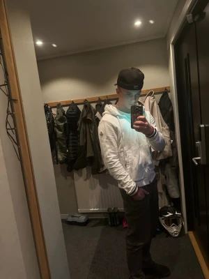 Vit hoodie med dragkedja från Moncler - Snygg vit hoodie från Moncler med dragkedja framtill, huva med dragsko och Moncler-logga på ärmen. NFC märket går att scanna. Perfekt för dig som gillar stilrena och exklusiva plagg.