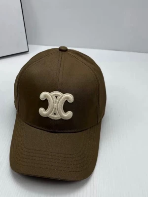 Brun keps från Celine med logga - Snygg brun keps från Celine med ikonisk vit broderad logga på framsidan. Klassisk böjd skärm och justerbar baksida. Materialet är slitstark bomull och kepsen har en stilren design som passar perfekt till streetwear och trendiga outfits.