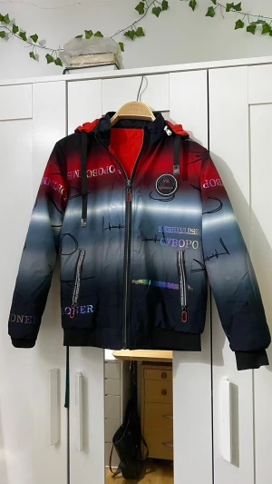 Färgstark vindjacka med tryck - Cool vindjacka med färgskiftning från rött till blått och svart, dekorerad med tryck och broderad patch på bröstet. Jackan har huva med dragsko, dragkedja framtill och två fickor med dragkedja. Insidan är röd och jackan har ribbade muddar. Som ni ser på bilden har den ingen storlek men jag gissar på att den är för barn mellan 8-10 år, annar kan ni själv avgöra ❤️