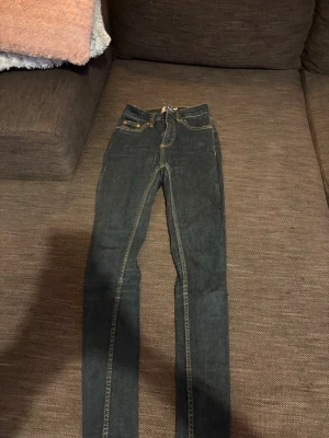 Mörkblå skinny jeans med kontrastsömmar - Snygga mörkblå skinny jeans med klassiska kontrastsömmar och femficksmodell. Jeansen har normal midja och raka ben, perfekta för en avslappnad men trendig look. Materialet är denim och de har dragkedja och knapp framtill.