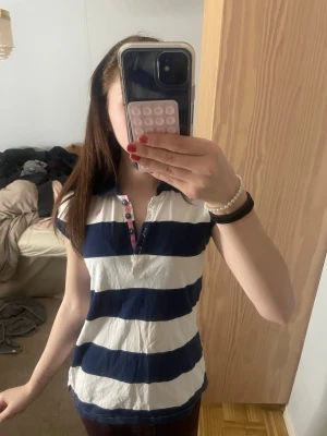 Randig pikétröja  - Säljer en kortärmad  med breda marinblå och vita ränder. Tröjan har klassisk krage, knappslå med rosa detaljer och en liten rosa logga på bröstet. Perfekt för en sportig och avslappnad look. Superfin för sommaren hör järna av dig för frågor!❤️