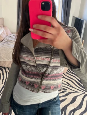 Grön jeansjacka  - Unik bikerjacka från F.A.M i grått med färgglada mönster i rosa, vitt och svart. Jackan har lång ärm, sned dragkedja och croppad passform. Materialet är en mix av bomull och polyester, perfekt för dig som vill sticka ut.