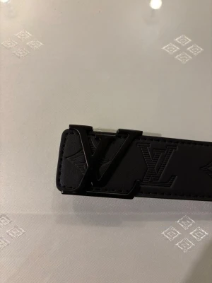 Svart bälte i skinn - Snyggt svart bälte med klassisk logga som spänne. Bältet är gjort i skinn och har diskreta mönsterpräglingar längs hela bandet. Perfekt accessoar för att lyfta din outfit med en exklusiv touch. 110cm. Allt i bilden följer med! Tveka inte att höra av er vid frågor eller funderingar😊