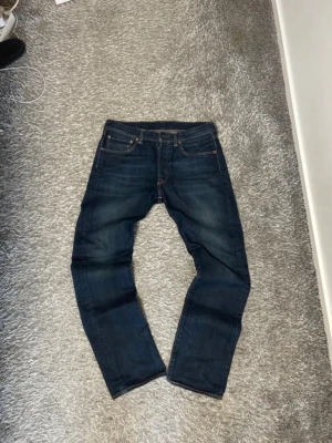 Mörkblå Levi's jeans herr - Säljer ett par klassiska mörkblå Levi's 501 jeans med raka ben och fem fickor. Jeansen har snygga kontrastsömmar och den ikoniska läderlappen bak i midjan. Tillverkade i slitstark denim som ger en tidlös look. Som nya, storlek 32/32. 
