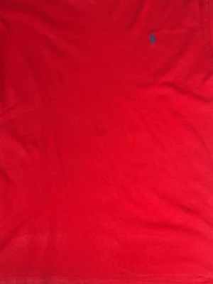 Röd t-shirt från Polo Ralph Lauren - Klassisk röd t-shirt från Polo Ralph Lauren med den ikoniska lilla blå loggan broderad på bröstet. T-shirten har rund halsringning och är tillverkad i mjuk bomull för en skön känsla. Perfekt till jeans eller shorts för en clean och enkel stil.