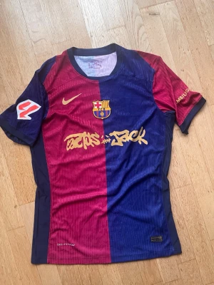 FC Barcelona matchtröja Lamine Yamal - Snygg FC Barcelona matchtröja från Nike i röd och blå med guldfärgade detaljer. Tröjan har klubbmärke, Nike-logga och 'Lamine Yamal 19' på ryggen. Tillverkad i lätt och ventilerande material, perfekt för fotboll eller träning.
