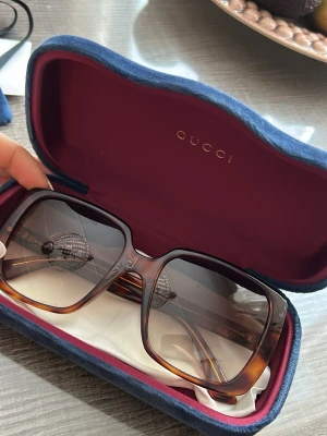 Gucci solglasögon - Säljer ett par snygga solglasögon från Gucci med stor fyrkantig form och bruna bågar i transparent acetat. Glasen är tonade och skalmarna har guldfärgade detaljer samt GG-logga på sidorna. Kommer med fodralet osv💙Helt oanvända