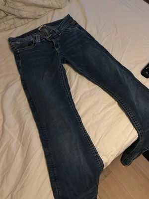 Blå bootcut jeans från Gina Tricot - Säljer ett par klassiska blå bootcut jeans från Gina Tricot. Jeansen har tydliga kontrastsömmar, normal midja och fem fickor. Materialet är slitstark denim i bomull. Perfekta för en avslappnad och trendig look.