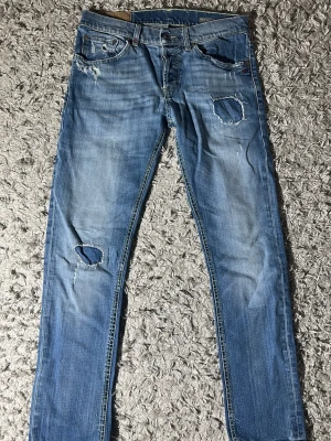 Blå dondup jeans med schyssta slitningar skinny fit - Säljer ett par blå jeans med slim fit och slitningar på både lår och knä. Jeansen har patchdetaljer och en klassisk femficksmodell. Perfekta för en avslappnad och trendig look.