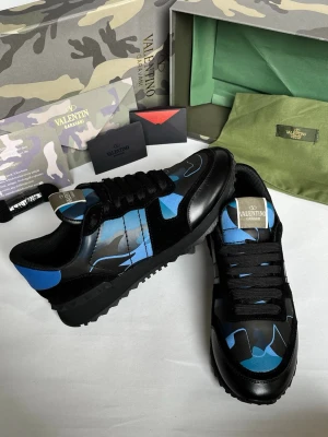 Valentino blå camo sneakers - Snygga sneakers från Valentino med blått och svart camomönster. Skorna har svarta snören, svarta detaljer i mocka och läder samt en robust sula. Perfekt för dig som vill sticka ut med en unik och trendig look.