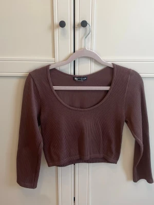 Brun ribbad croppad topp från Zara - Säljer en brun ribbad croppad topp från Zara med rund ringning och trekvartsärm. Perfekt för dig som gillar en enkel men trendig stil. Materialet är mjukt och stretchigt, vilket gör den bekväm att bära. Storlek M-L men liten i storlek. Passar en S eller S-XS. L