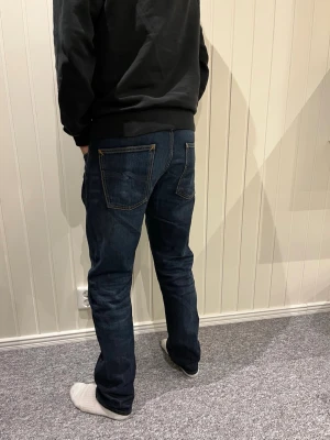 Mörkblå raka jeans herr - Säljer ett par mörkblå jeans med raka ben och klassisk femficksdesign. Jeansen har kontrastsömmar och normal midja. Perfekta för dig som gillar en enkel och stilren look. Materialet är denim i bomull.