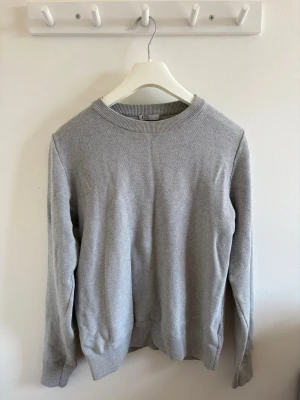 Herr grå stickad sweatshirt  - En stilren grå stickad tröja med rund hals och långa ärmar. Den har ribbade muddar och är lätt att matcha med olika outfits. I storlek S från Cubus. 