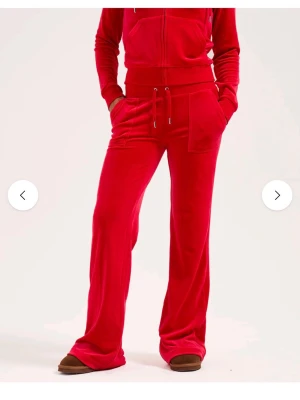 Röda velourbyxor Juicy Couture - Mysiga röda velourbyxor från Juicy Couture med bred resår i midjan och dragsko. Byxorna har raka ben, stora fickor framtill och diskret logga på ena fickan. Perfekta för chill dagar hemma eller när du vill vara extra bekväm. Dom är sparsamt använda men inte nyskick!