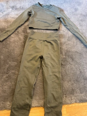 Olivgrönt ribbat set från HM - Snyggt olivgrönt set från HM  med långärmad crop top och matchande höga tights. Setet är ribbat och har en tight passform som framhäver figuren. Perfekt för dig som gillar stilrena och bekväma underkläder i mjukt material stl xs 