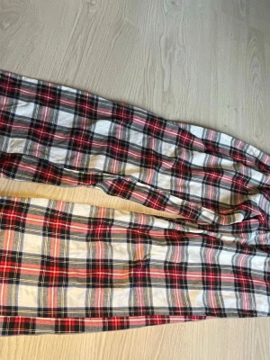 Rutiga pyjamasbyxor från Gina Tricot - Säljer ett par klassiska rutiga pyjamasbyxor från Gina Tricot i mjuk bomull. Byxorna har ett mönster i rött, svart, vitt och blått och är perfekta för mysiga hemmakvällar. Resår i midjan för extra komfort.
