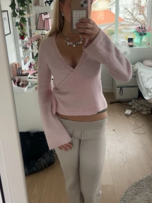 Ljusrosa omlottstickad tröja - Supersöt ljusrosa stickad omlottopp med djup V-ringning och långa, lite utsvängda ärmar. Tröjan knyts i sidan och har en mjuk, fluffig känsla. Perfekt för dig som gillar en feminin och trendig look. Sitter super fint!