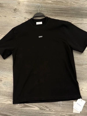 Svart Off-White t-shirt - Svart t-shirt från Off-White med liten vit 'OFF'-text på bröstet och stort grafiskt tryck i vitt och grått på ryggen. 